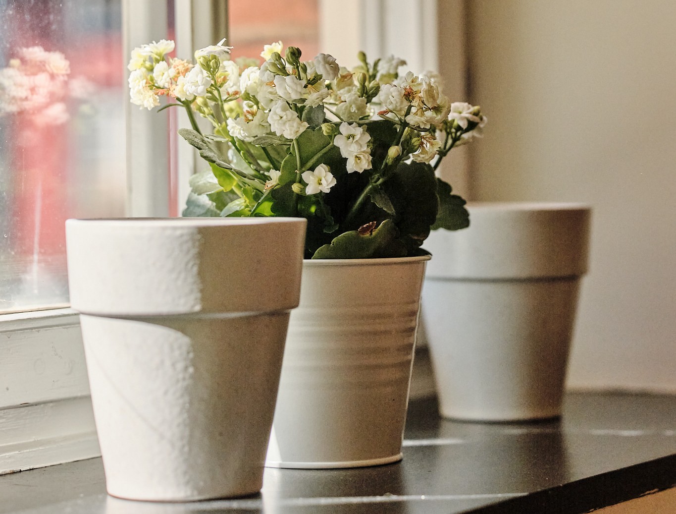 Bild på tre grå blomkrukor på en fönsterbräda